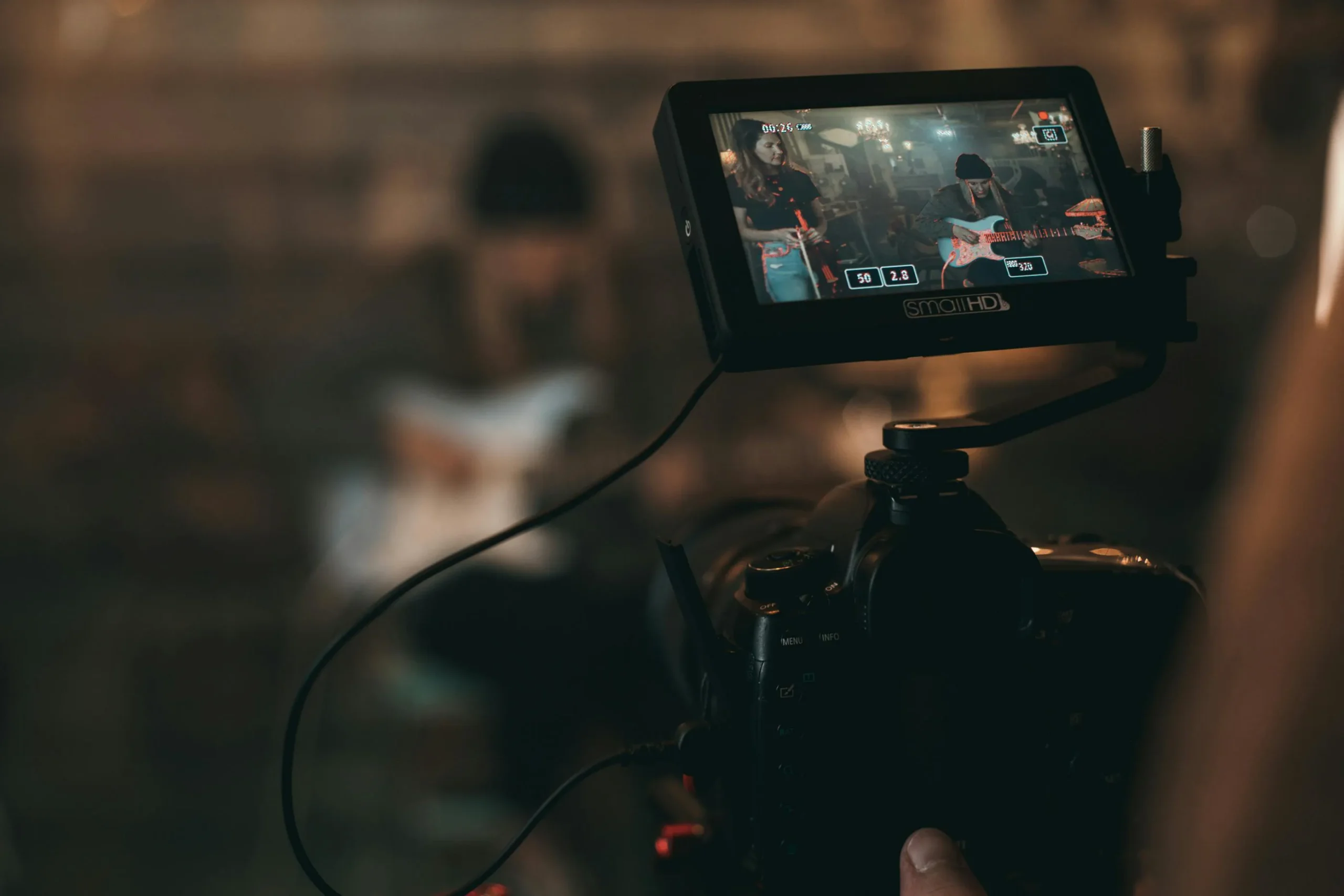 Close-up view of a professional video camera with an external monitor displaying musicians playing guitar in a dimly lit studio