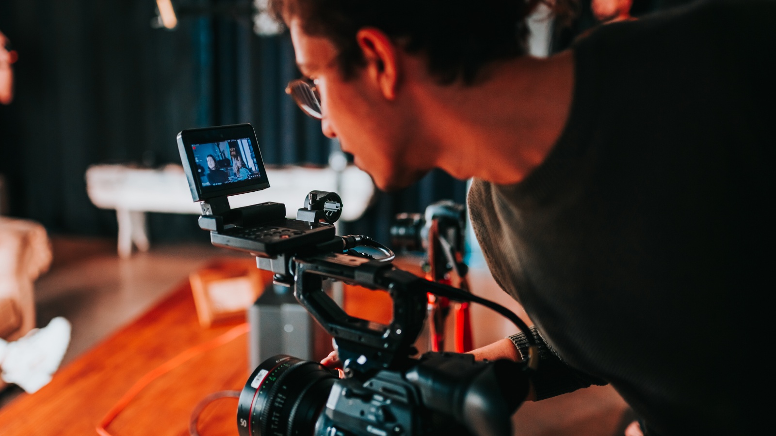 A videographer looking at a camera's small viewfinder monitor