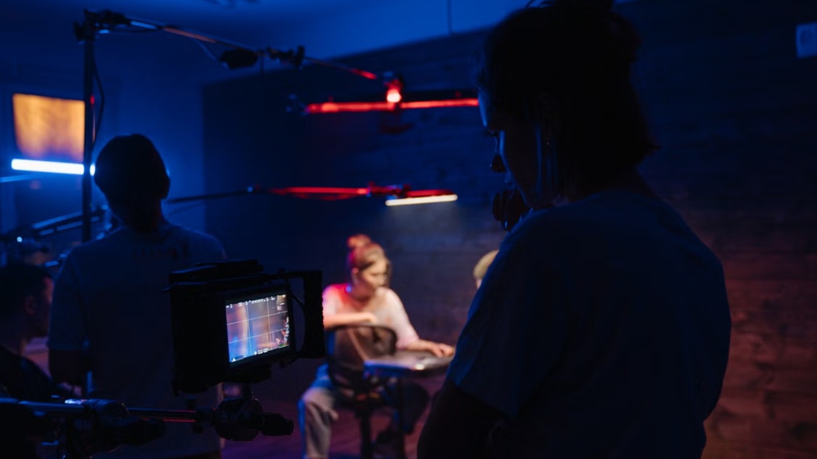 A film crew silhouette stands in the foreground observing a lit production set