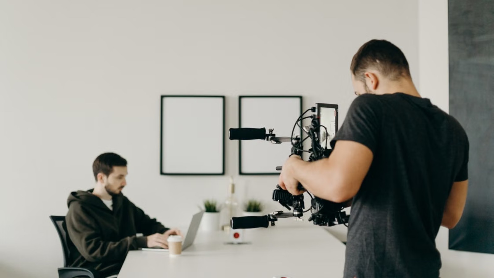 A videographer operates a large camera rig, filming a man working on a laptop